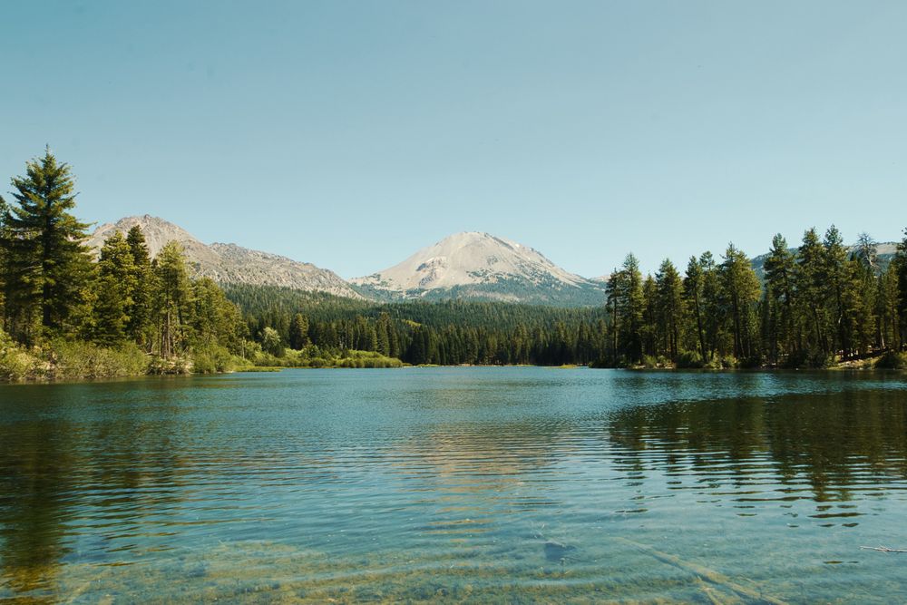 Clear mountain lake surrounded by pine forest with a peak in the distance