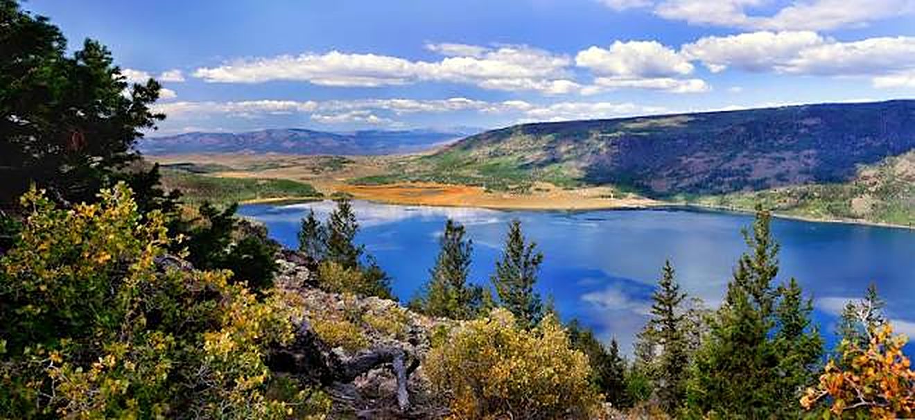 Fish Lake from above with blue water ringed by pine forest and golden hills