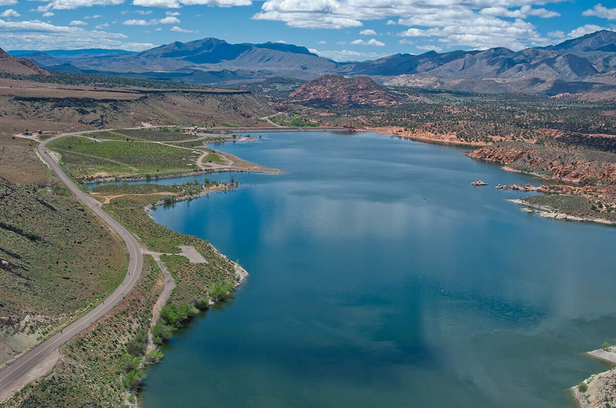 Aerial view of Gunlock Reservoir with blue water, a winding road and red rock hills